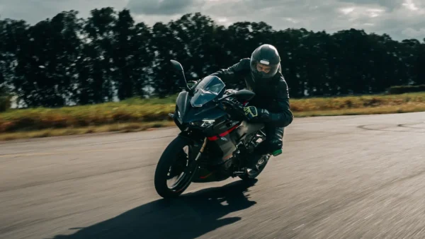 Motociclista pilotando uma Shineray SBM 250S preta com detalhes vermelhos, inclinada em uma curva na pista de asfalto.