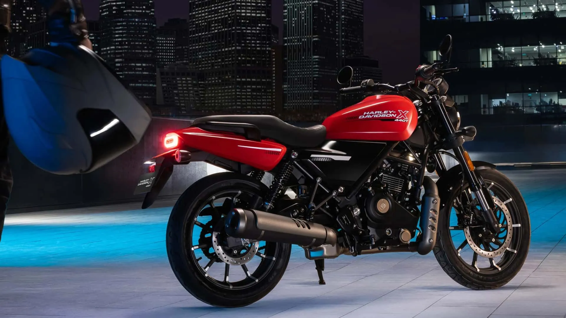 Harley-Davidson X440 vermelha vista de lado, com motor monocilíndrico de 440 cc, rodas de liga leve e escapamento preto, em cenário urbano noturno.